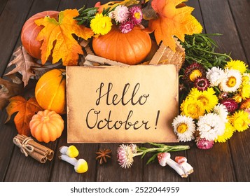 A sheet of paper with the inscription hello October, a bouquet of chrysanthemum flowers, pumpkins, autumn leaves, a yellow scarf. Hello October concept