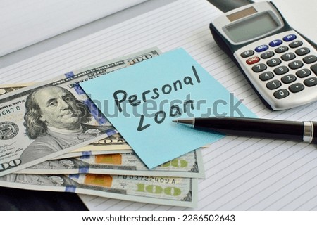 Sheet of paper with the words Personal Loan on an office desk with a calculator, notepad, pen and US dollars