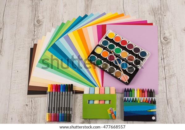 Sheets of colored paper,
iridescent palette of colored paper, rainbow colors, rainbow
colors, watercolors, wax crayons, colored markers, crayons on the
wooden table