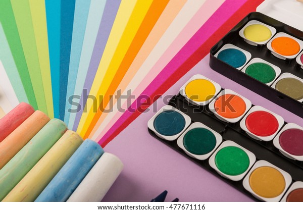 Sheets of colored paper,
iridescent palette of colored paper, rainbow colors, rainbow
colors, watercolors, wax crayons, colored markers, crayons on the
wooden table