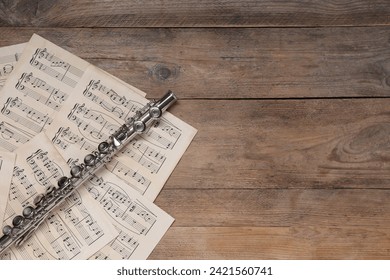Sheets with musical notes and flute on wooden table, flat lay. Space for text