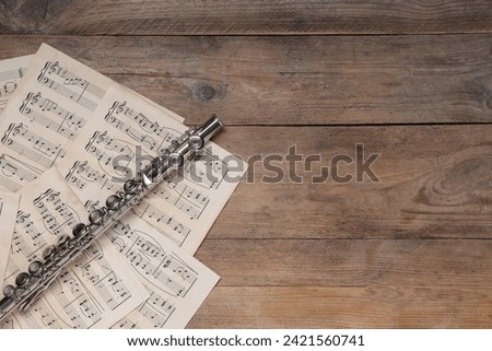 Sheets with musical notes and flute on wooden table, flat lay. Space for text
