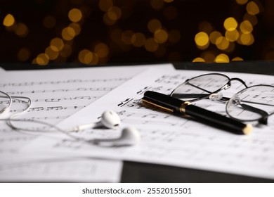 Sheets of musical notes, glasses, earphones and pen on table against blurred lights, closeup. Bokeh effect - Powered by Shutterstock