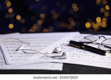 Sheets of musical notes, glasses, earphones and pen on table against blurred lights, closeup. Bokeh effect - Powered by Shutterstock