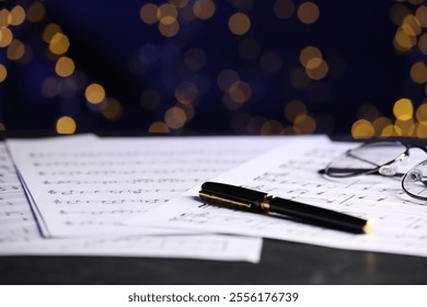 Sheets of musical notes, glasses and pen on table against blurred lights, closeup. Bokeh effect - Powered by Shutterstock