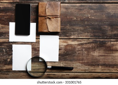 sheets of paper, leather notebook, mobile phone and magnifier on a wooden table