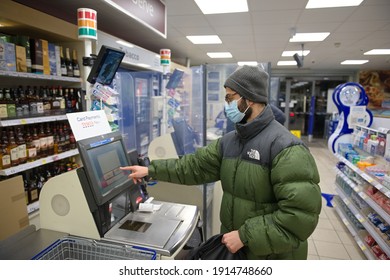 Sheffield, United Kingdom, 14th January, 2021: Young Man Wearing A Face Mask And Winter Clothes Pays For Groceries At A Tesco Express Self Checkout