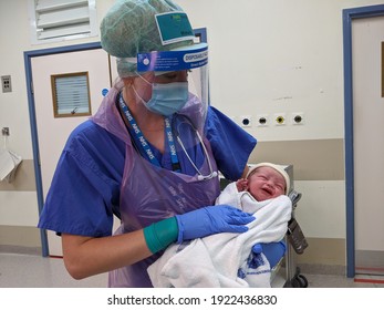 SHEFFIELD, UNITED KINGDOM - MAY 8th 2020: A midwife in Sheffield's Jessops Hospital holds a newborn baby while wearing full PPE during the Coronavirus Pandemic.