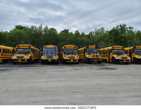 Shelburne, NS,\
CAN, July 8, 2021 - A school bus depot with a line of different\
styled school buses parked in a single file, horizontal line with\
the front of the buses facing\
forward.