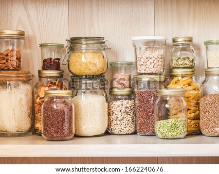 Shelf in the kitchen with various cereals and seeds - peas split, sunflower and pumpkin seeds, beans, rice, pasta, oatmeal, couscous, lentils,  bulgur in glass jars 