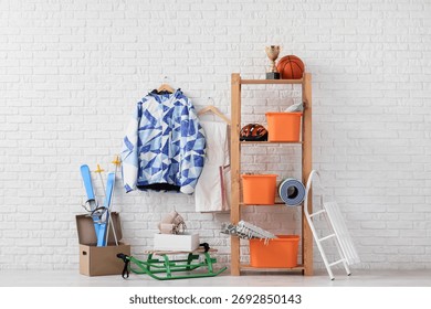 Shelf unit with different stuff and sleds near white brick wall in room