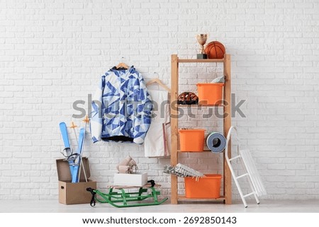 Shelf unit with different stuff and sleds near white brick wall in room