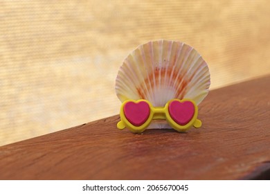 Shell and tiny sunglasses on wooden table. Vacation concept.
