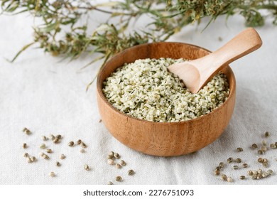 Shelled hemp seeds as superfoods , supplement for eat with fiber and omega 3. Crushed cannabis seeds in wooden bowl with spoon and dried buds of plant on hemp fabric.