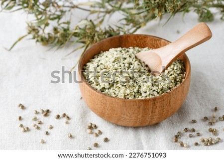 Shelled hemp seeds as superfoods , supplement for eat with fiber and omega 3. Crushed cannabis seeds in wooden bowl with spoon and dried buds of plant on hemp fabric.