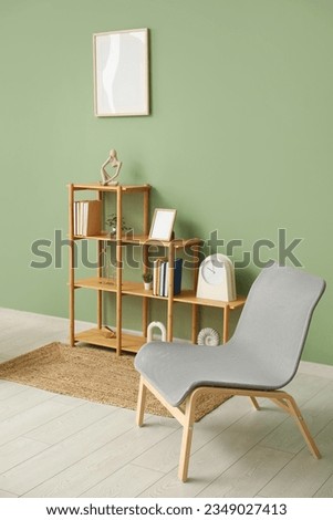Shelving unit with books, decor, chair and blank frame hanging on green wall in room