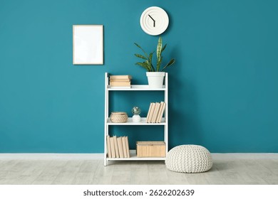 Unidad de estantería con libros, planta de casa y puf cerca de la pared azul