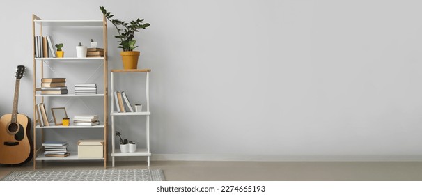 Shelving unit with books, houseplants and guitar near light wall in room. Banner for design - Shutterstock ID 2274665193