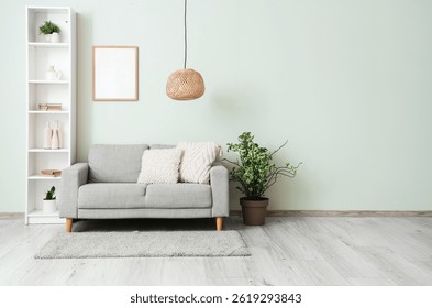 Estantería con sofá, planta de casa y marco de fotos cerca de la pared gris en la sala de estar