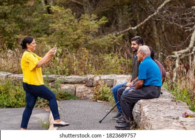 Shenandoah Valley, VA, USA 09-27-2020: An Indian Family Visiting Shenandoah Valley Is Posing For A Family Picture. The Mother Takes The Photo Of Her Dad And Teenager Kids With Her Smart Phone. 