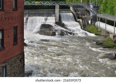 SHERBROOKE, QUEBEC, CANADA - MAY 6, 2022 - Magog River Sherbrooke Abenakis Hydroelectric Power Plant Dam. Large White Penstock And Footbridge