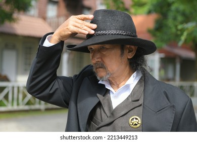 The Sheriff Dressed In A Uniform With The Sheriff's Star Badge, He Is Raising His Hand To Take Off His Leather Brimmed Hat.