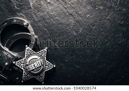 Sheriff star and handcuffs on black slate table closeup. Law concept background