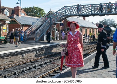 Sheringham, Norfolk, UK - SEPTEMBER 14 2019: Woman In Fancy Red Vintage Dress With Hat And Umbrella Smiles At Camera At Train Platform During 1940s Weekend