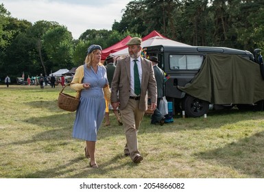 Sheringham, Norfolk, UK - SEPTEMBER 14 2019: Couple in 1940s vintage clothes holding a whisker basket walk on grass during the 40s weekend