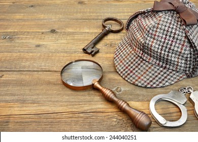 Sherlock Holmes Cap famous as Deerstalker, Old Key, Real Handcuffs and Vintage Magnifying Glass on Grunge Wooden Table - Shutterstock ID 244040251