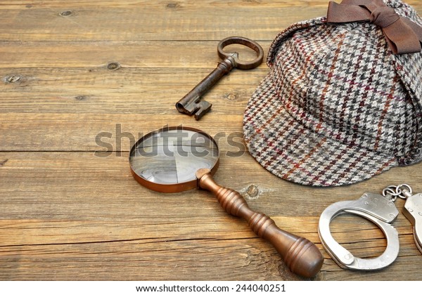 Sherlock\
Holmes Cap famous as Deerstalker, Old Key, Real Handcuffs and\
Vintage Magnifying Glass on Grunge Wooden\
Table