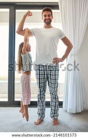 Shes always on my arm. Full length shot of an adorable little girl hanging from her fathers bicep at home.