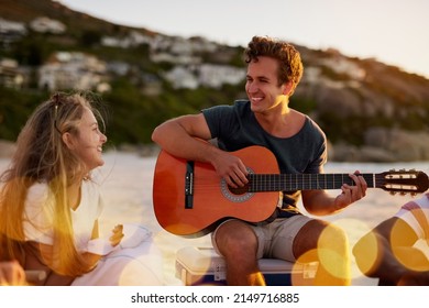 Shes my inspiration. Shot of a man playing the guitar while sitting on the beach with his girlfriend. - Powered by Shutterstock