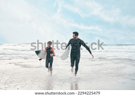 Shes ready to ride his own ripple. Shot of a man and his young son at the beach with their surfboards.