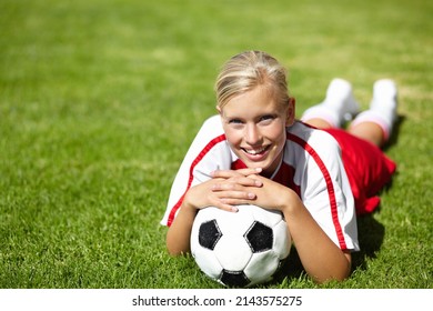 Shes The Team Captain. Portrait Of An Attractive Female Football Player Lying Chest Down On The Grass And Leaning On A Soccer Ball.