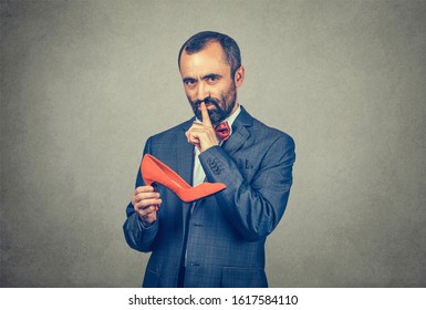 Shh. Sly Bearded Businessman Man Holding A Red Shoe, Making Silence Gesture With Hand Looking At Camera. Mixed Race Bearded Model Isolated On Gray Studio Background. Confidentiality, Business Secret