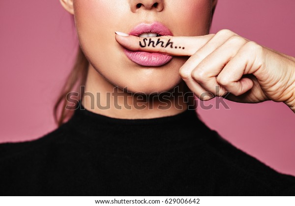 Shh! Women's secrets. Cropped shot of female with finger in mouth. Closeup portrait of young woman is showing a sign of silence with shhh written on the finger.