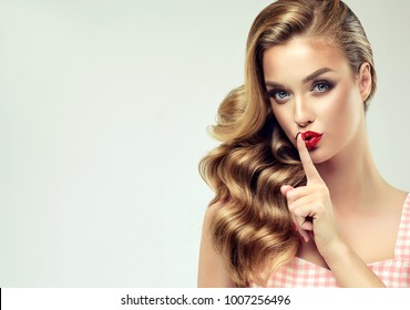 Shhhhh . Beautiful girl with bright makeup and curly hair telling a secret .Portrait  happy woman who is calling to someone .Funny girl model  whispering about something. Expressive facial expressions