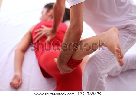 Shiatsu back and leg massage on female patient dressed in red.