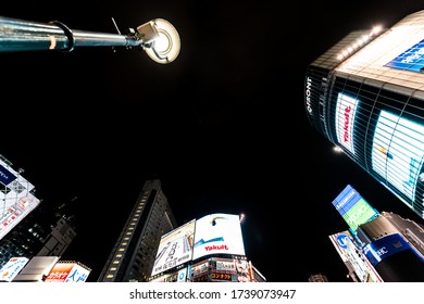 Shibuya, Japan - April 1, 2019: Famous Crossing In Downtown Tokyo City With Neon Billboard Lights Low Angle View Cityscape And Commercial Advertisements At Night