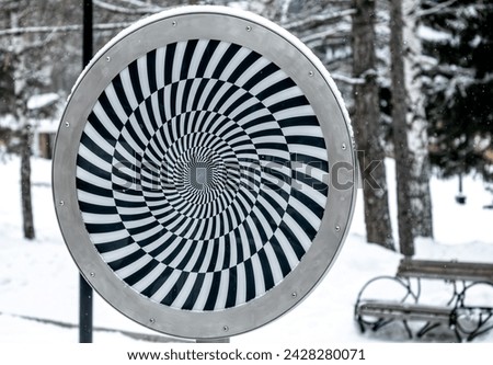 A shield with an optical illusion of black and white stripes.
