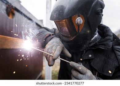 Shielded metal arc welding. Worker welding metal with electrodes, wearing protective helmet and gloves. Close up of electrode welding and electric sparks - Powered by Shutterstock