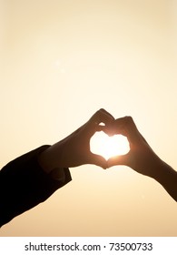 Shiloutte of two hands join to form a heart shape with sun beam inside the heart