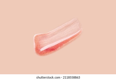 Shimmering lip gloss sample on a beige background. Smudged pink lip gloss with glitters.