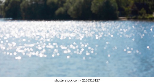 Shimmering in the sun lake or river surface in the sunny day and bushes in the bank. Natural defocus lights with bokeh blur background. Summertime, aqua, pure water, impoundment, ecological issue