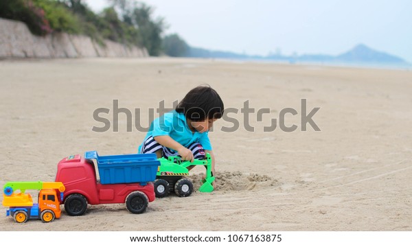 Shin - Playing with plastic car excavator toys\
on a sand at a sea beach with\
joy.