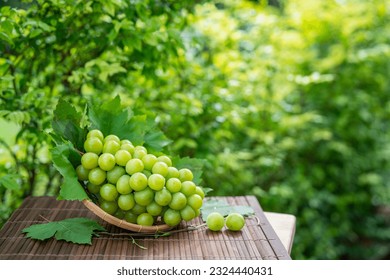 Shine Muscat Grape with leaves in blur background, Green grape in Bamboo basket on wooden table in garden.