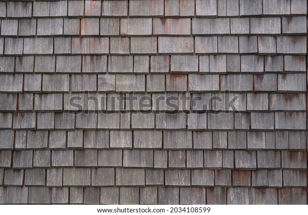 Shingle wooden tile facade background.Texture of\
old weathered wooden tiled roof or surface of natural veneer wall\
backdrop. Eco background. Environmental conservation,eco-friendly\
house concept