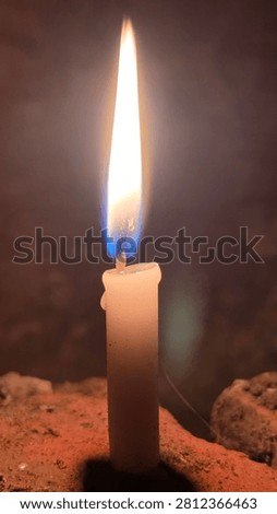 Shining candle flame throwing warm light on raw brick corner inside dark cottage room