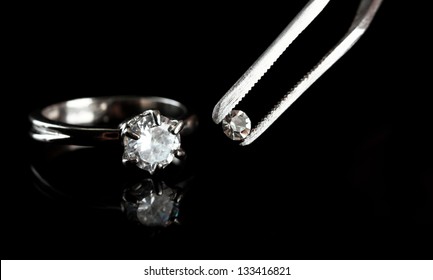 Shining crystal (diamond) in the tweezers and ring, on black background